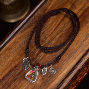 Medicine Buddha braided rope necklace with silver charms and red beads displayed on wooden surface, overhead flat lay view