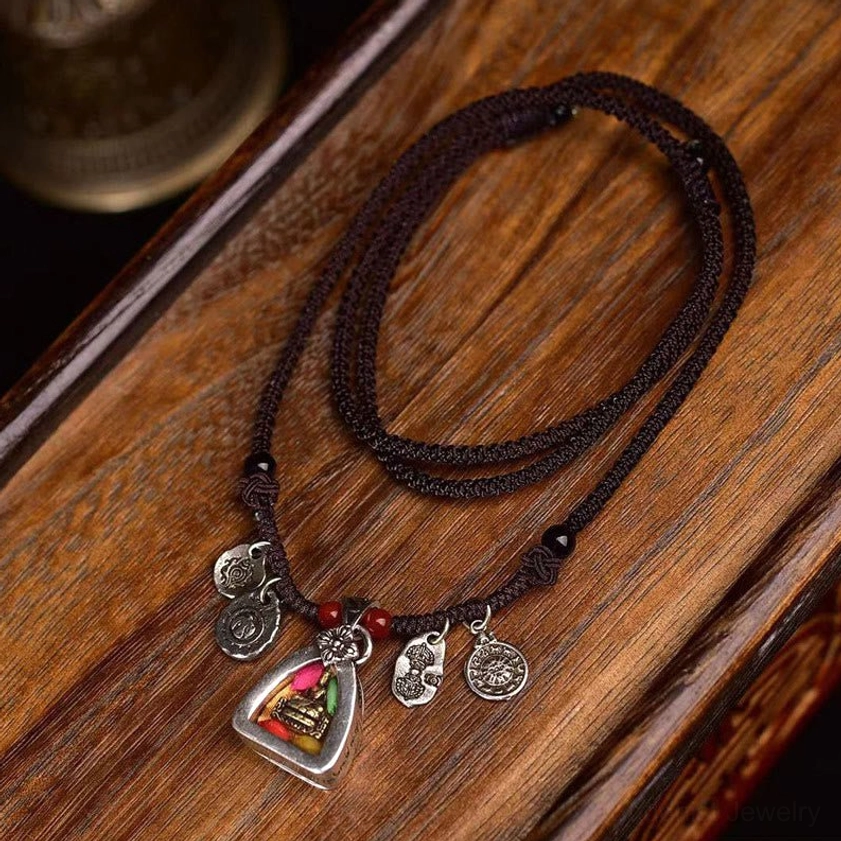 Medicine Buddha braided rope necklace with silver charms and red beads displayed on wooden surface, overhead flat lay view