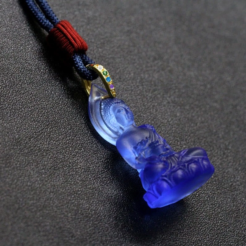 Medicine Buddha pendant necklace displayed on bright red surface showing full cord and pendant styling