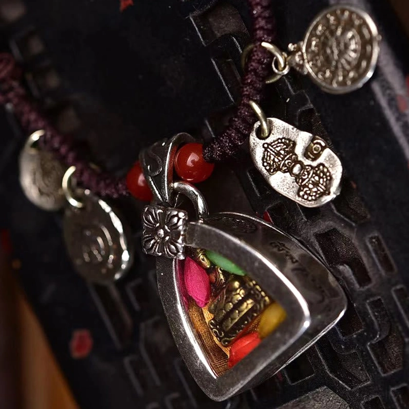 Medicine Buddha braided rope necklace with multiple silver decorative charms and red bead accents on carved wooden surface