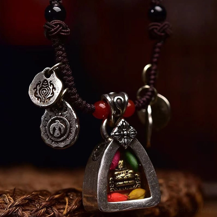 Side profile of Medicine Buddha pendant with black top beads and engraved silver dangle charms on dark background