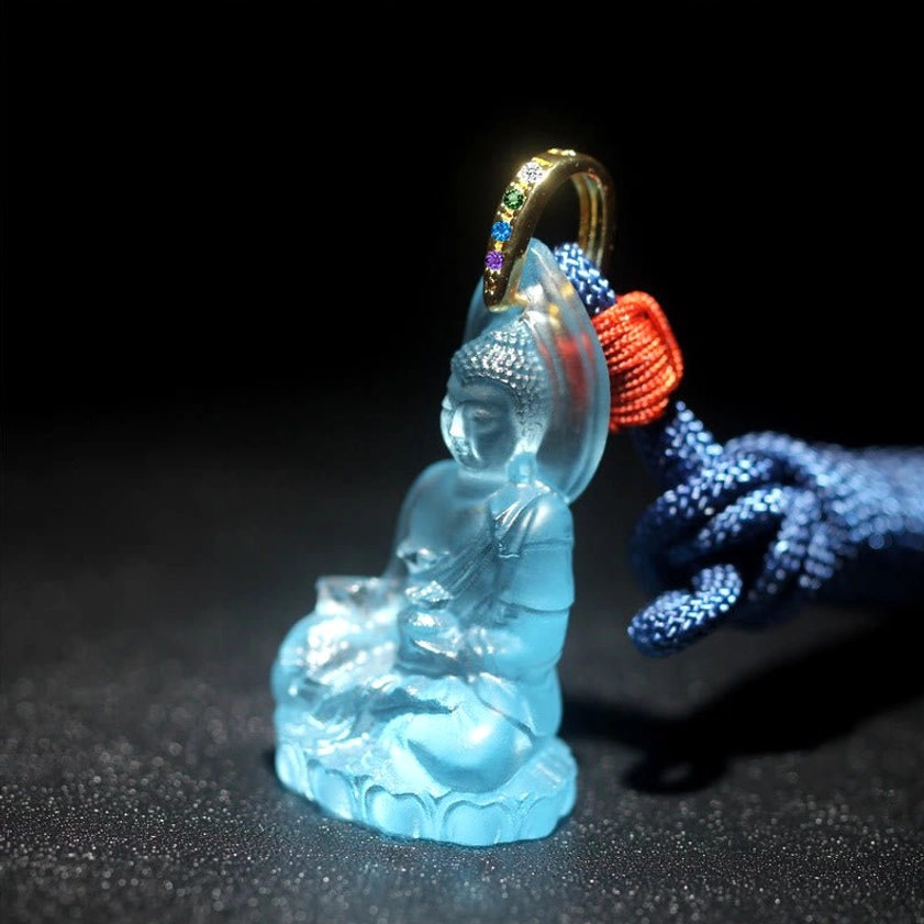 Seated Medicine Buddha glass pendant three-quarter side view with blue woven lanyard and ritual vessel detail