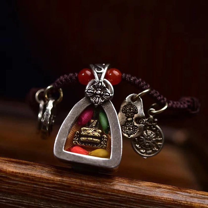 Front close-up of Medicine Buddha pendant necklace showing silver floral ornament with paired red beads on wooden surface