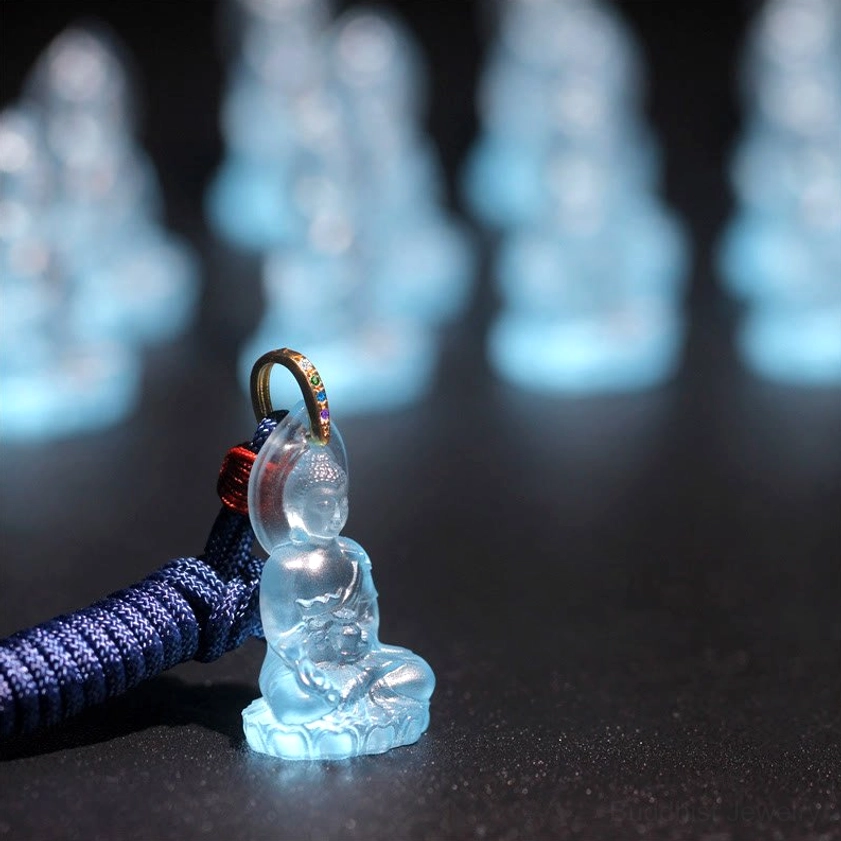 Single translucent blue Medicine Buddha Liuli crystal pendant with red lanyard knot on black background