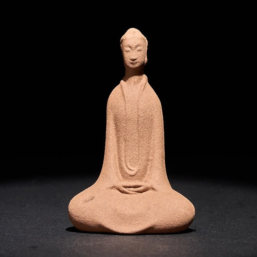 Cross-legged ceramic Buddha statue with hands folded in meditation position, warm earthy brown color on dark background