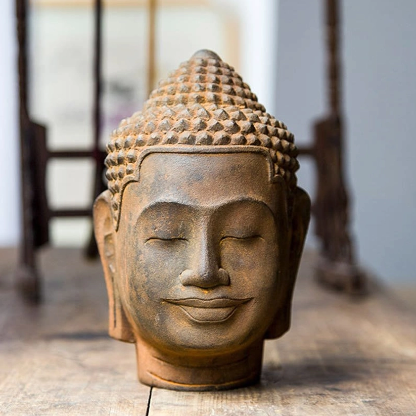 Meditating Buddha head statue with closed eyes and serene expression, front view on wooden table, rust-cast iron powder resin finish