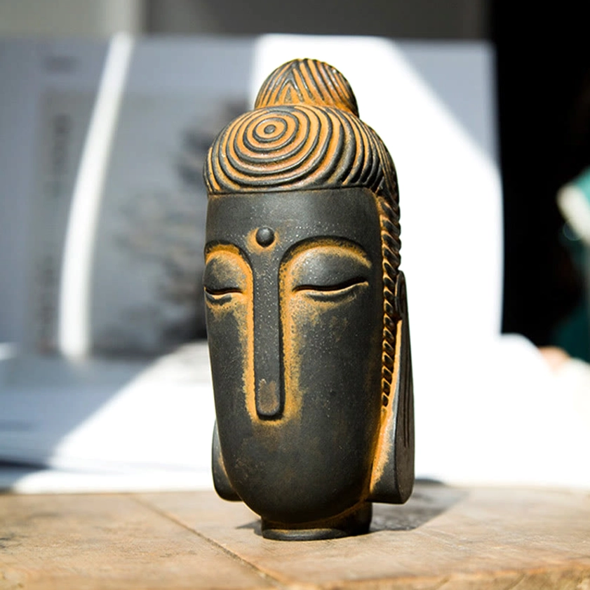 Meditating Buddha statue with closed eyes and rust patina finish on wooden desk with open books