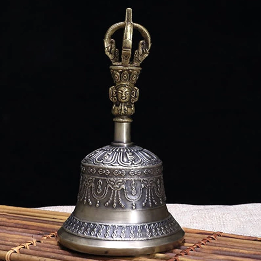 Single polished copper meditation bell with intricate carved handle finial on linen mat wooden table setting