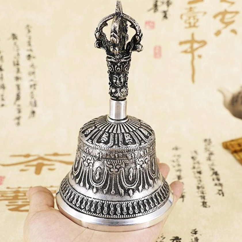 Hand holding handcrafted Buddhist meditation bell with carved vajra handle and embossed decorative patterns