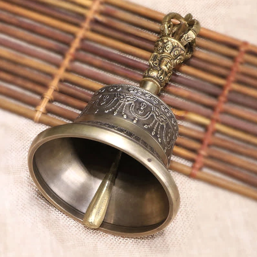 Side profile view of copper meditation bell showing internal clapper and engraved patterns on bamboo mat surface