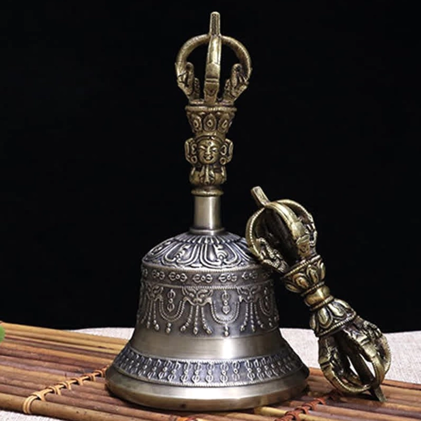 Buddhist meditation bell with carved handle and matching vajra dorje on bamboo mat background, displaying intricate embossed decorative patterns