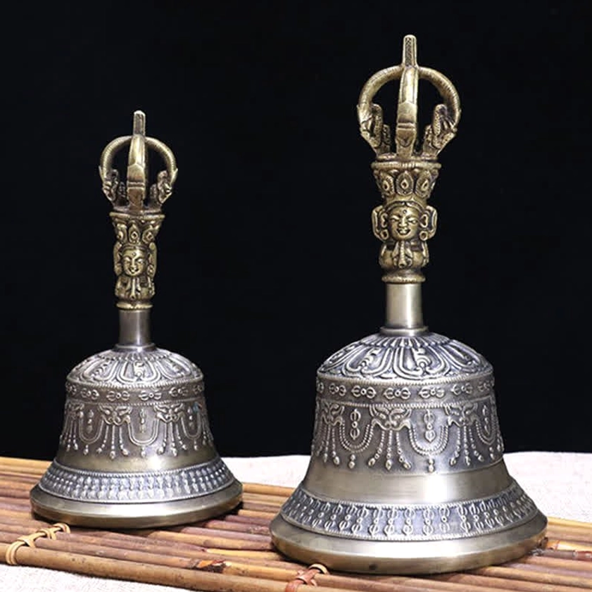 Pair of handcrafted copper meditation bells with symmetrical embossed decorative patterns on bell bodies against bamboo mat and black background