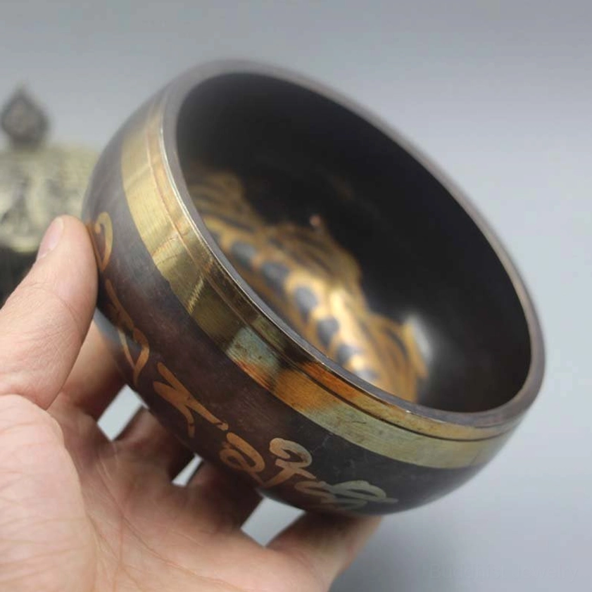 Handcrafted Buddhist singing bowl held in hand showing dark bronze body with golden script and gold-banded rim against neutral background