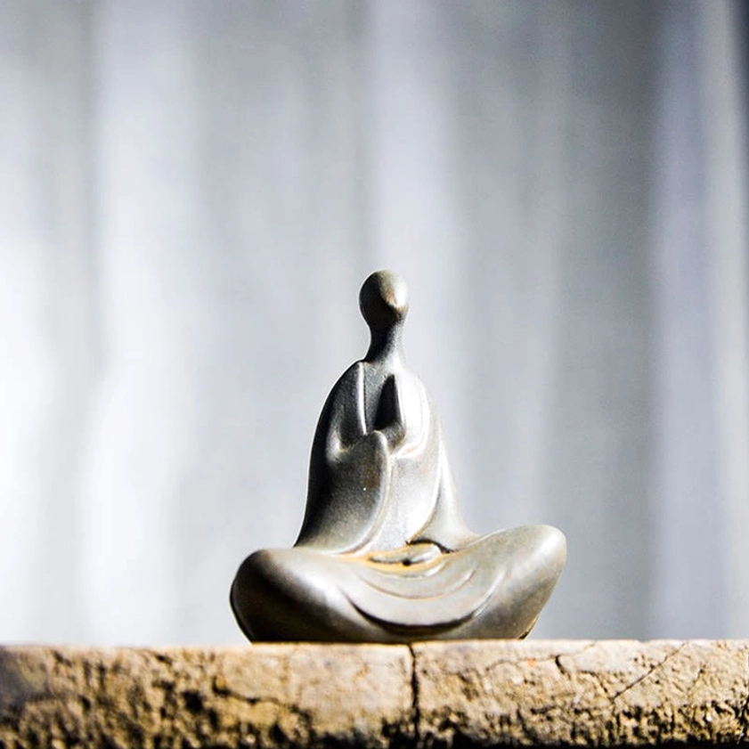 Meditation Buddha sculpture with clasped hands in dark brownish matte tone displayed against fabric backdrop