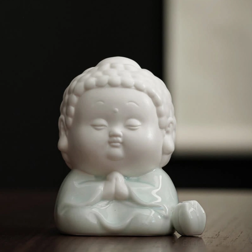 Frontal view of prayer-pose ceramic Buddha incense burner with clasped hands, white body and glazed robes on wooden surface