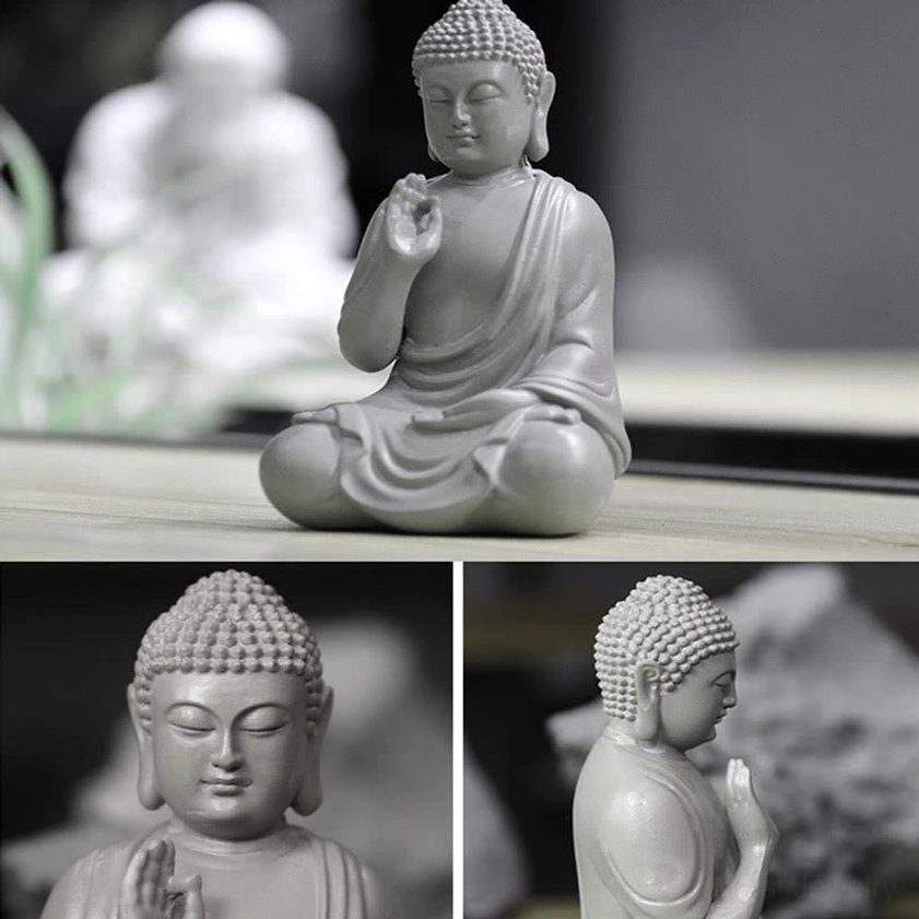 Compact classic seated Buddha resin statue in matte light gray shown in medium shot on display table with blurred decor background