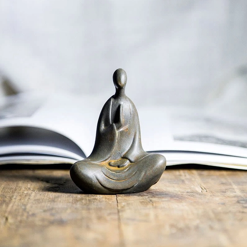 Minimalist meditation Buddha statue in dark bronze finish displayed on wooden desk beside open book