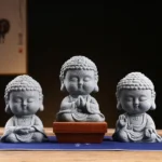 Set of 3 handcrafted meditation Buddha statues in grey sandstone with varied sacred postures displayed on wooden tea table