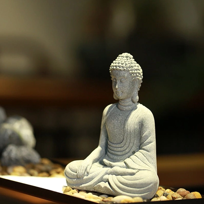 Handcrafted sandstone Buddha decoration on zen gravel display tray with warm ambient lighting, side profile view