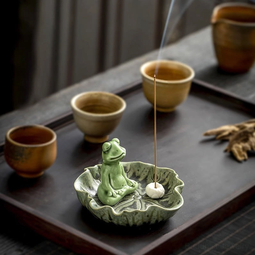 Frog ceramic incense burner on wooden tea table with burning incense and brown ceramic tea cups