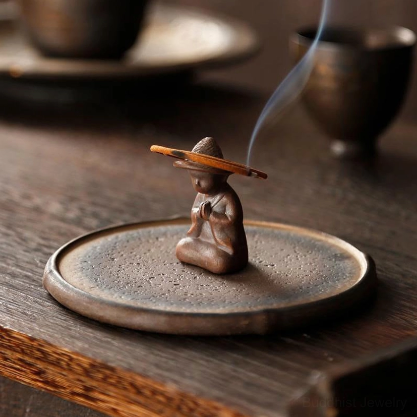 Handcrafted ceramic monk incense burner with burning sandalwood incense on wooden tea table, showing rising fragrant smoke for meditation and spiritual practice