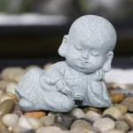 Handcrafted reading monk Buddha statue with natural sandstone finish on pebble stones - miniature zen sculpture