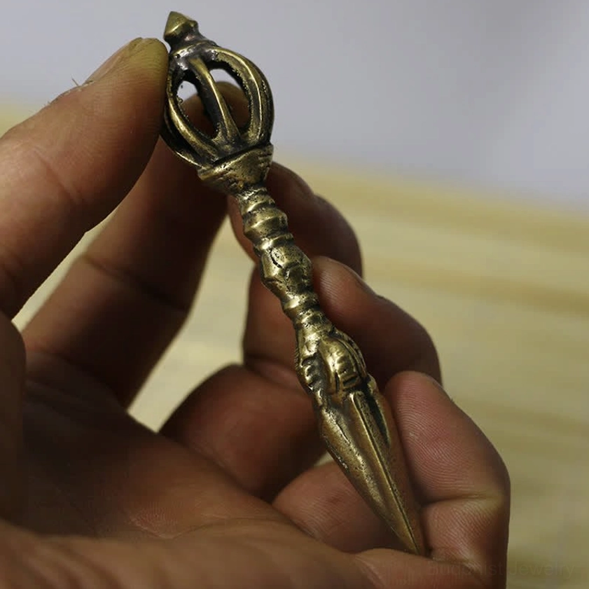 Compact handcrafted copper vajra held in hand overhead, showing antique brass tone and delicate carved patterns for meditation practice