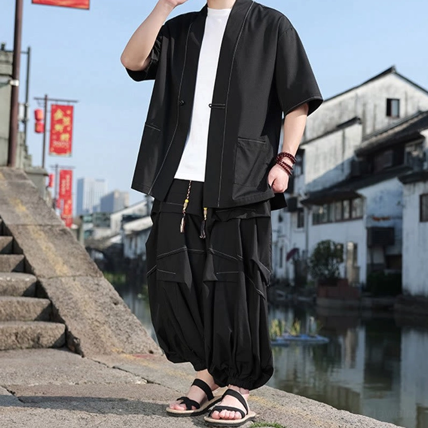 Black kimono jacket with frog button closure worn with hand in pocket, showing woven wrist bracelet detail