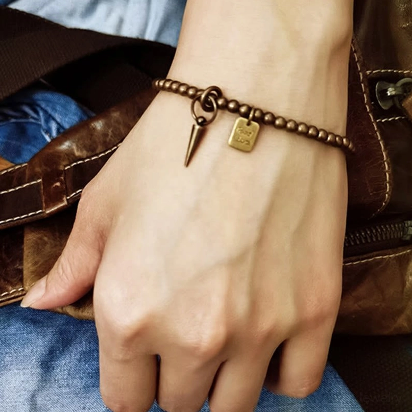 Men's hand wearing brass Good Luck bracelet - lifestyle scene with leather bag and denim background