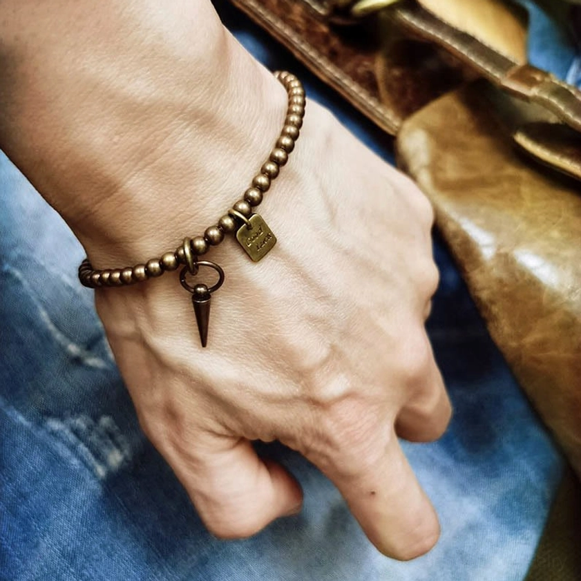 Men wearing vintage brass Good Luck bracelet with cone pendant - wearable lifestyle shot with denim and leather accessories