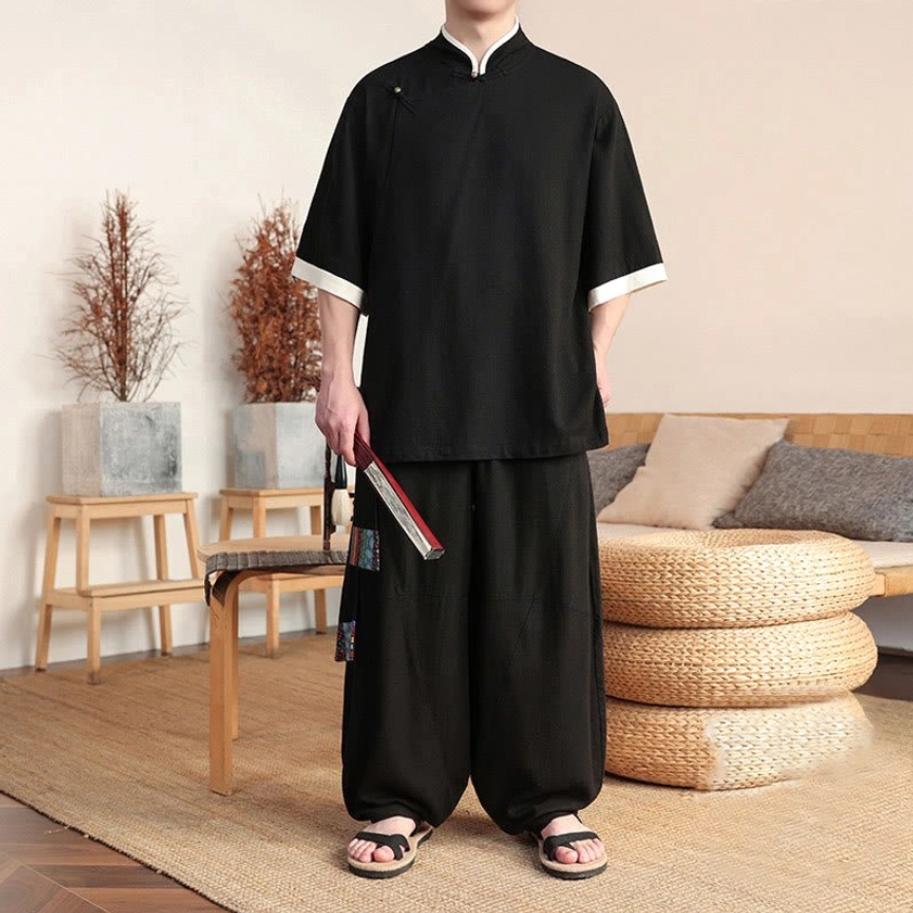 Man wearing black Buddhist meditation suit holding folding fan, showcasing relaxed fit