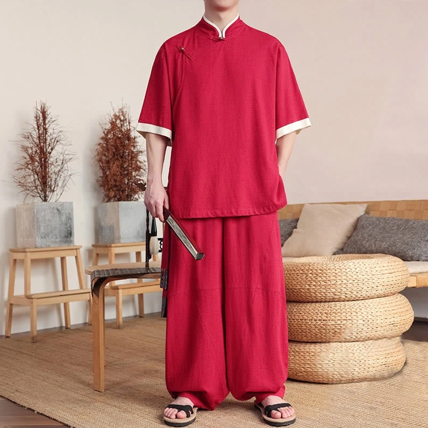 Man in red Buddhist meditation suit holding folding fan, displaying wide-leg pants and white sleeve accents