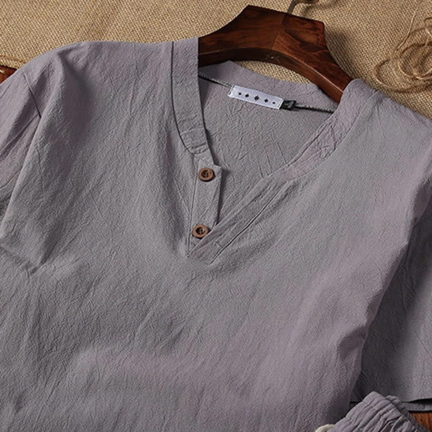 Light gray henley collar meditation top for men hanging on wooden hanger, close-up view
