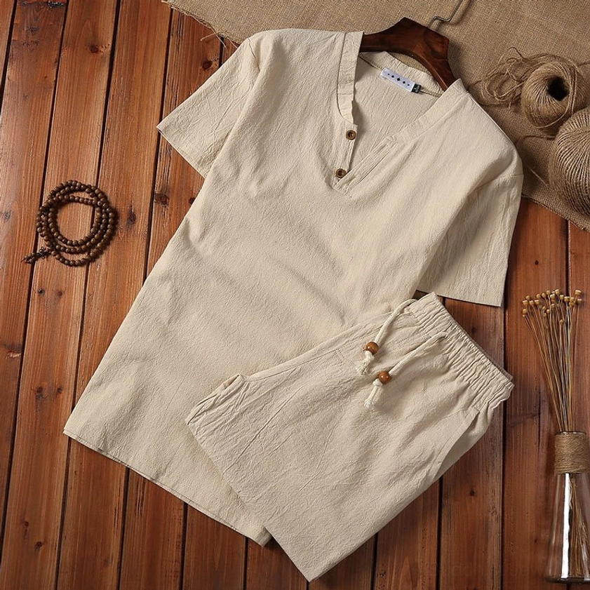 Beige men's cotton linen meditation suit set with henley collar top and drawstring shorts, flat lay on wooden table