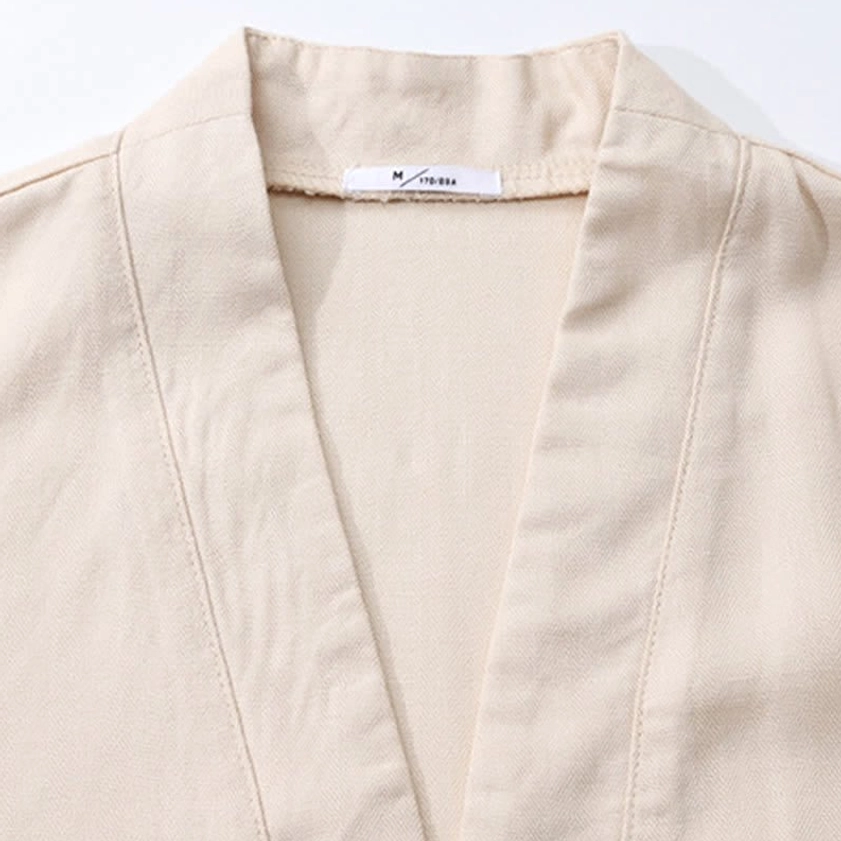 Close-up detail of cream woven cotton fabric V-neck neckline stitching of men's meditation shirt with brand label
