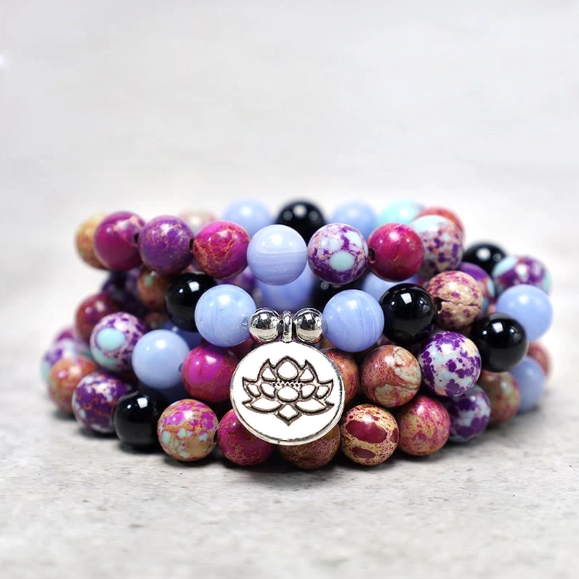 Multiple purple Miano stone lotus malas stacked together featuring central large silver lotus pendant and natural stone beads