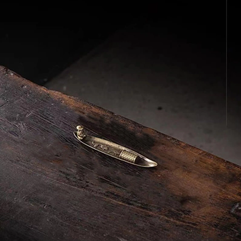 High angle side view of compact mini boat incense holder on dark wooden surface, bronze metal with embossed details