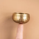 Mini handmade brass singing bowl held on fingertip showing hammered finish and ringed rim for Buddhist meditation