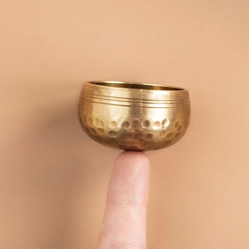 Mini handmade brass singing bowl held on fingertip showing hammered finish and ringed rim for Buddhist meditation