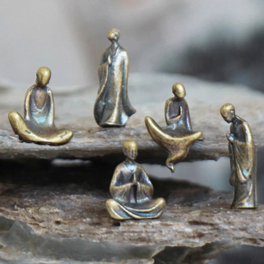 Four miniature bronze Buddha statues with diverse meditation postures and aged metal texture on flat rock slab base, overhead shot