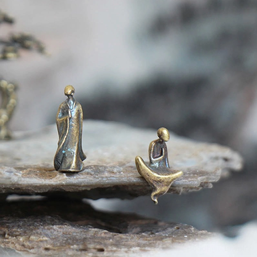 Mini bronze Buddha statues in different poses - standing and reclining meditation monks on rock slab, three-quarter side view with ink-wash background