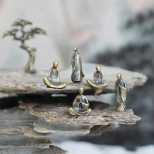 Mini bronze Buddha statues set displayed on layered rock with miniature pine tree, overhead view showing five distinct meditation poses
