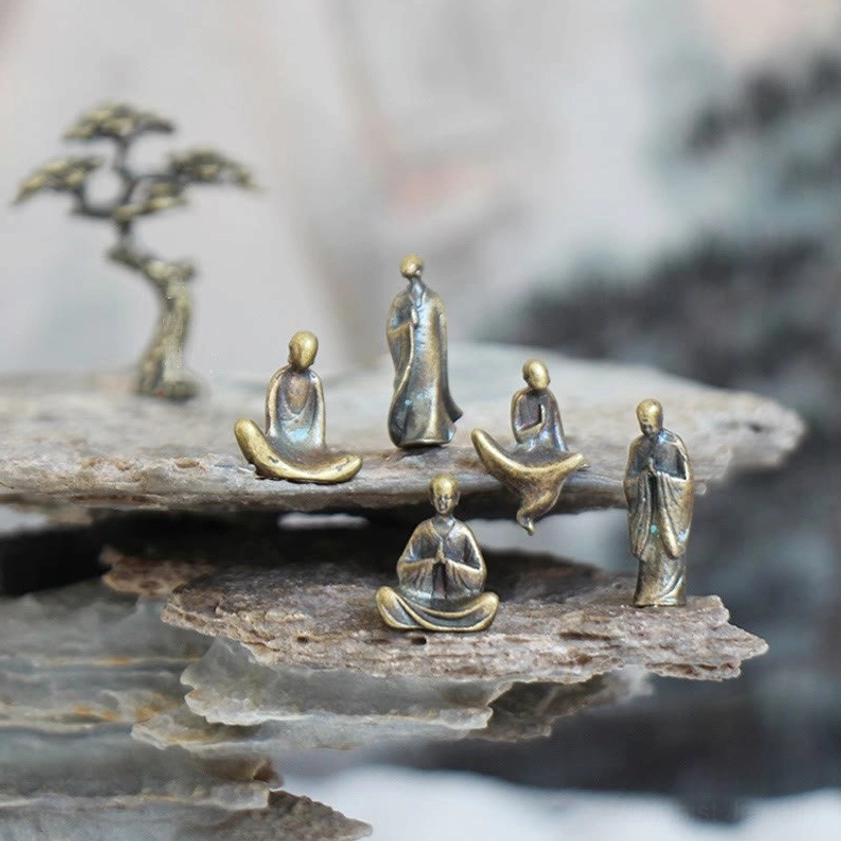 Mini bronze Buddha statues set displayed on layered rock with miniature pine tree, overhead view showing five distinct meditation poses