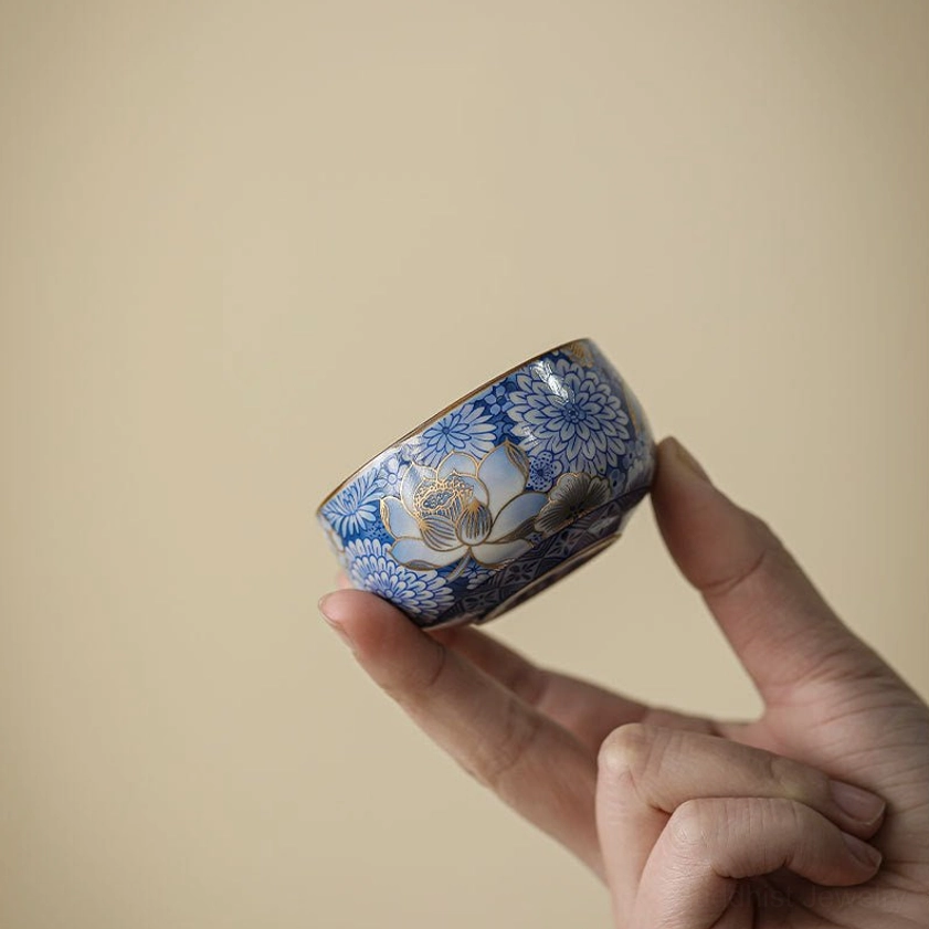 Mini delicate porcelain tea cup with hand-painted gilt floral patterns between thumb and finger