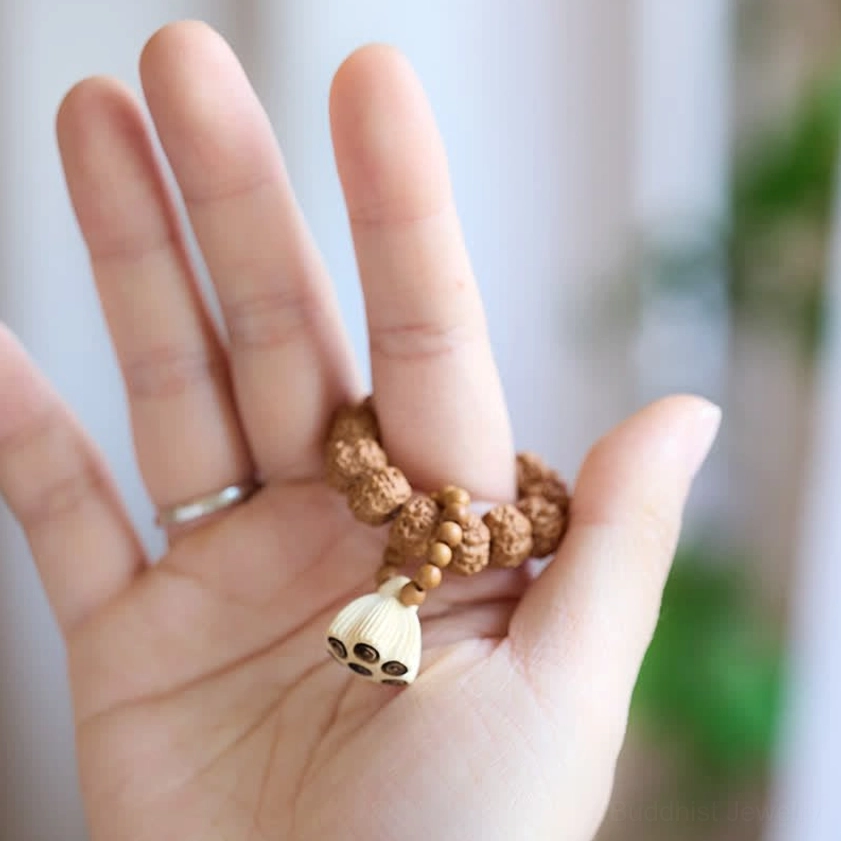 Flat lay top-down view of mini vajra seed lotus bracelet on open palm showing brown beads and carved lotus charm