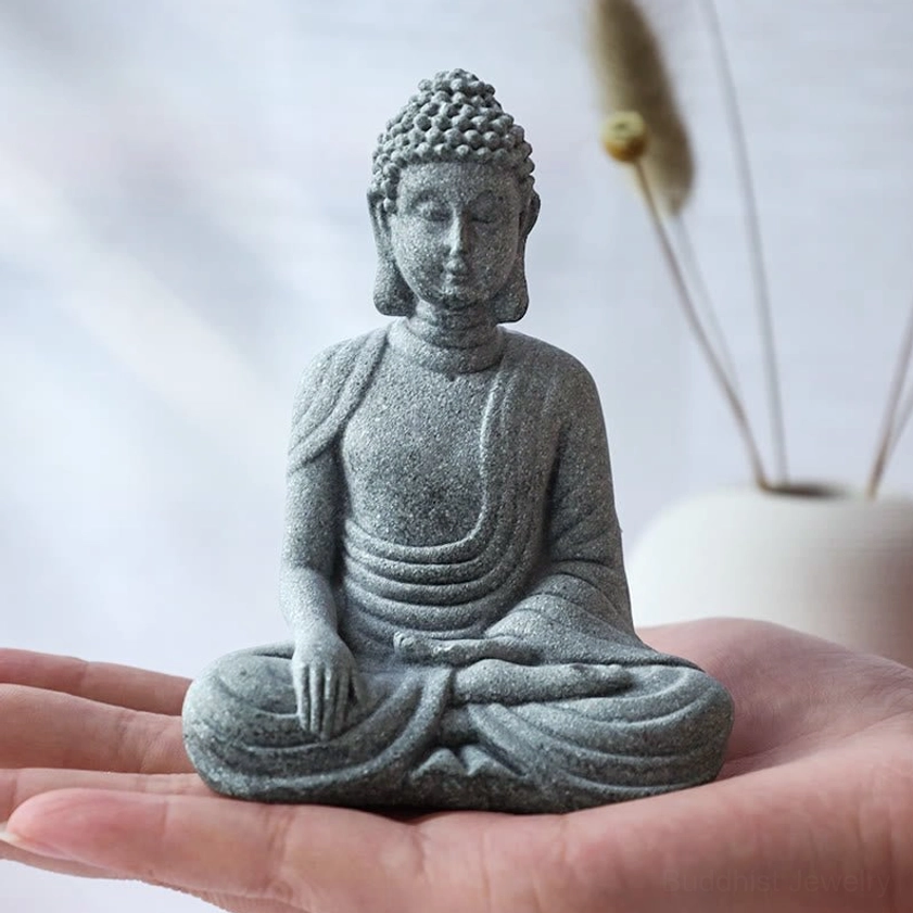 Hand-sculpted small sandstone Buddha statue in meditation pose, close-up eye-level view showcasing fine craftsmanship details