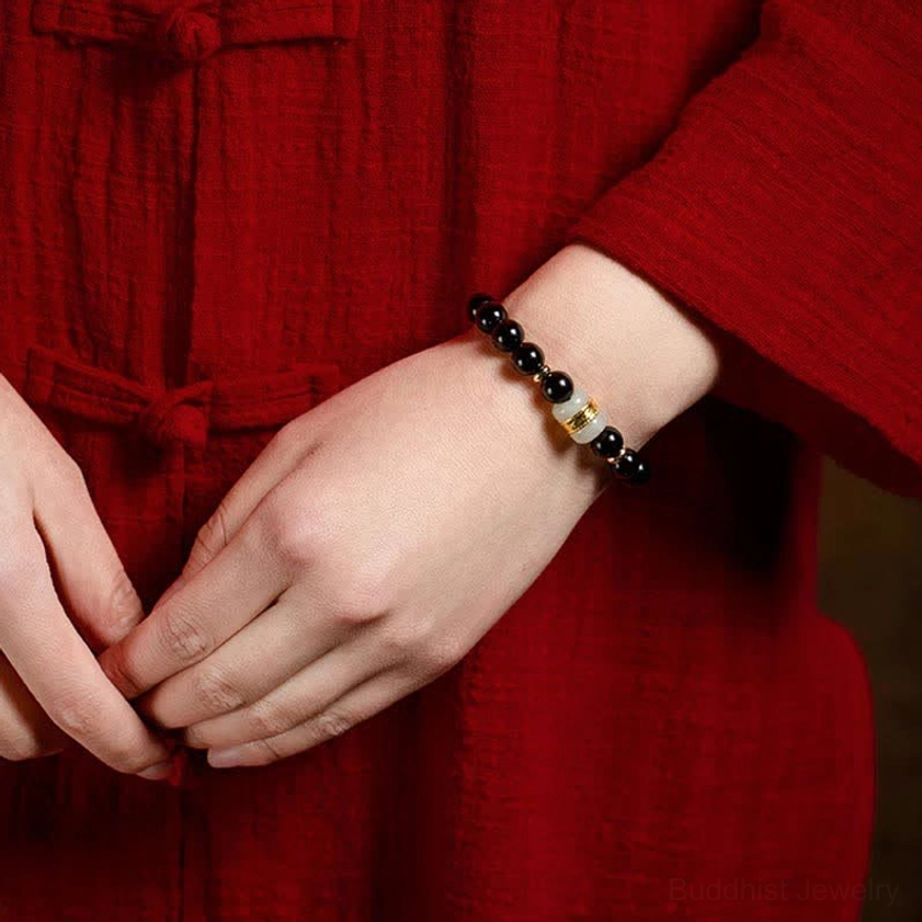 Minimalist black obsidian and jade Buddhist bracelet in two-hand side view with traditional red Chinese attire, highlighting slim profile and elegant gold-jade spacer design