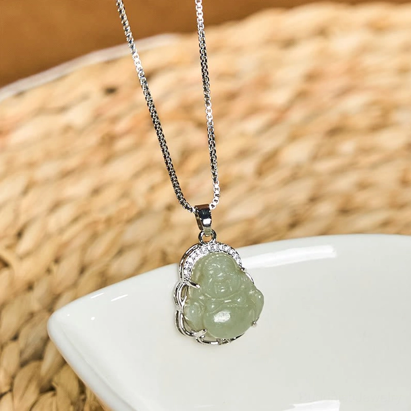 Mint green natural Hetian jade Buddha pendant necklace with silver-toned metal trim and crystal accents, flat lay on white ceramic dish - authentic Buddhist jewelry for abundance