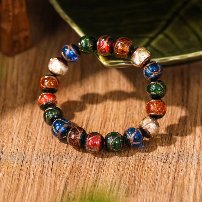 Mixed multicolor liuli glass Buddhist bracelet with metallic line patterns viewed from side angle on wooden surface