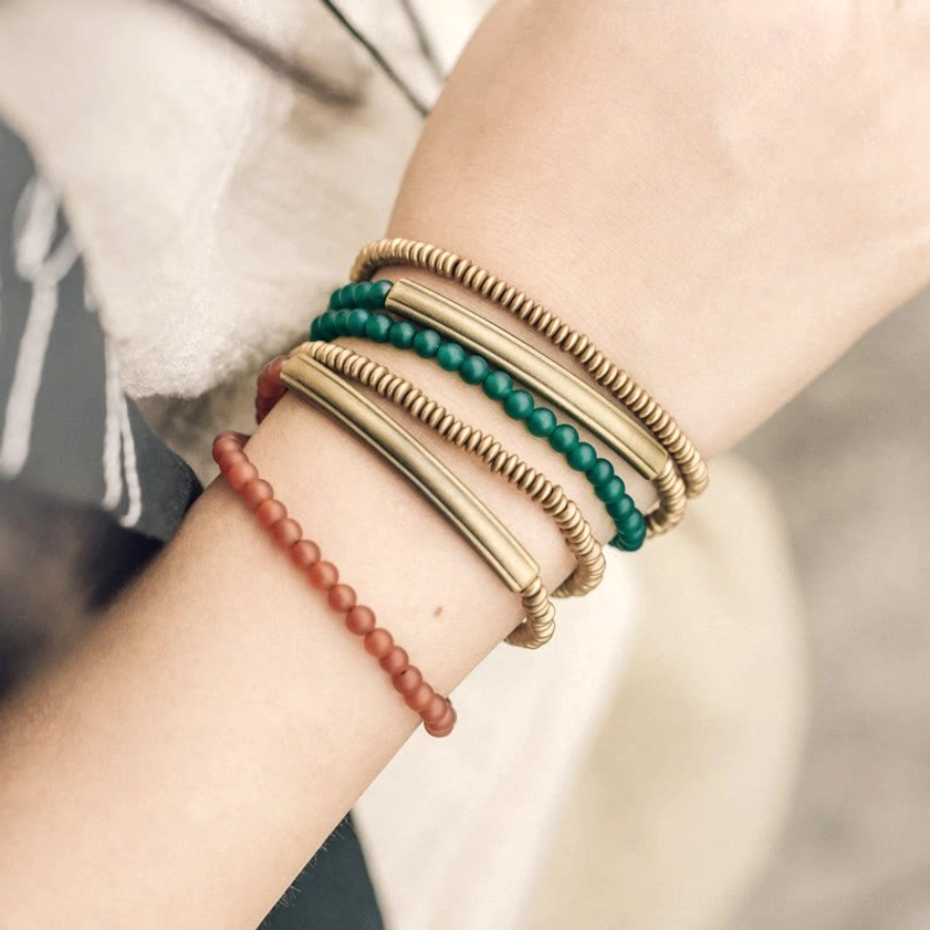 Mixed multi-stone Buddhist bracelet set worn on both wrists showing layered stacking style with red agate green agate copper metal bangles and brass components
